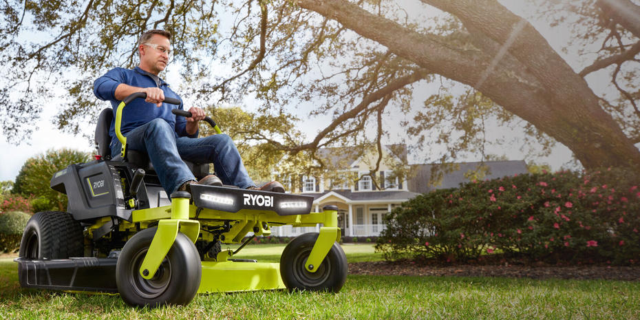 Man on RYOBI ride on mower wearing safety glasses in front of a large white house
