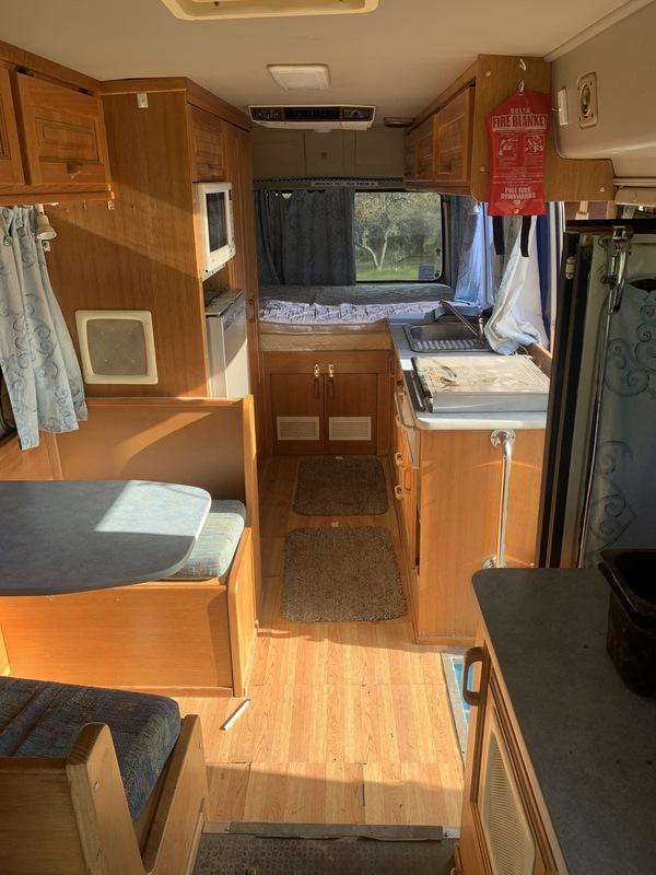 Interior of older campervan, looking from front past table, kitchen and to bed. 