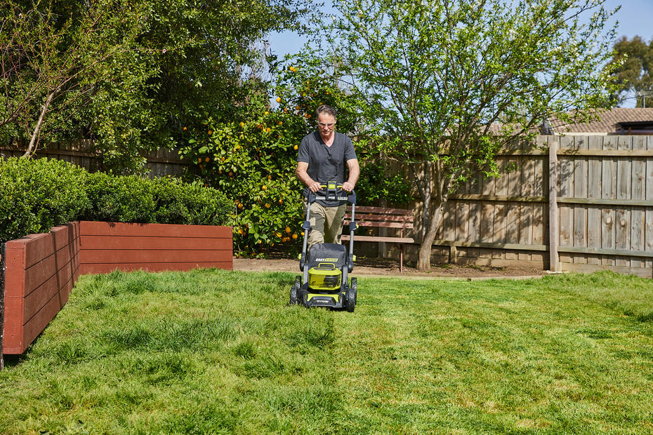 A man uses a Ryobi lawn mower to trim the grass in his backyard