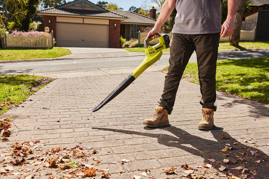 A man wearing a Ryobi leaf blower to clear the driveway of leaves