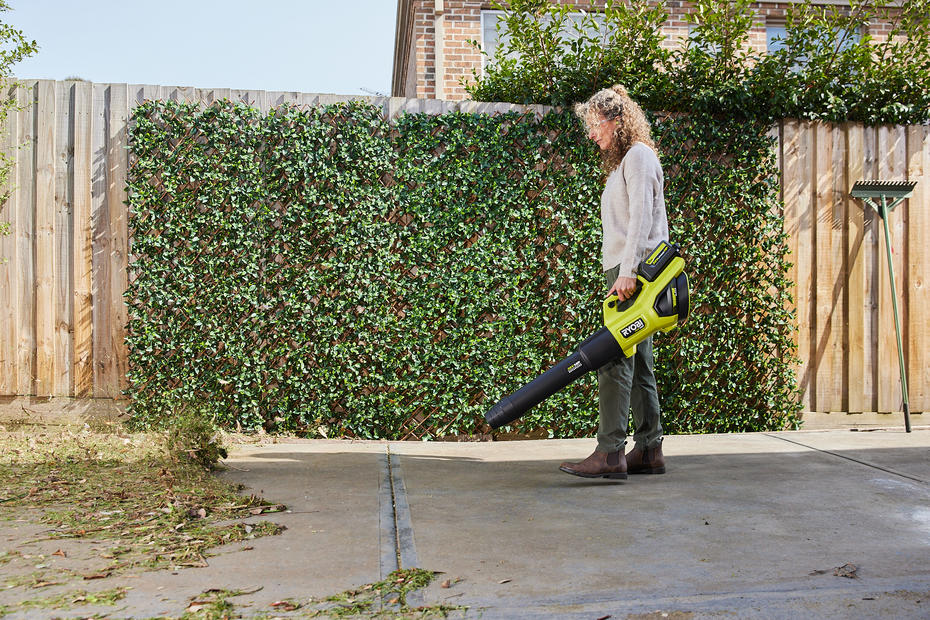 A woman uses a Ryobi 36V leaf blower to clear her driveway