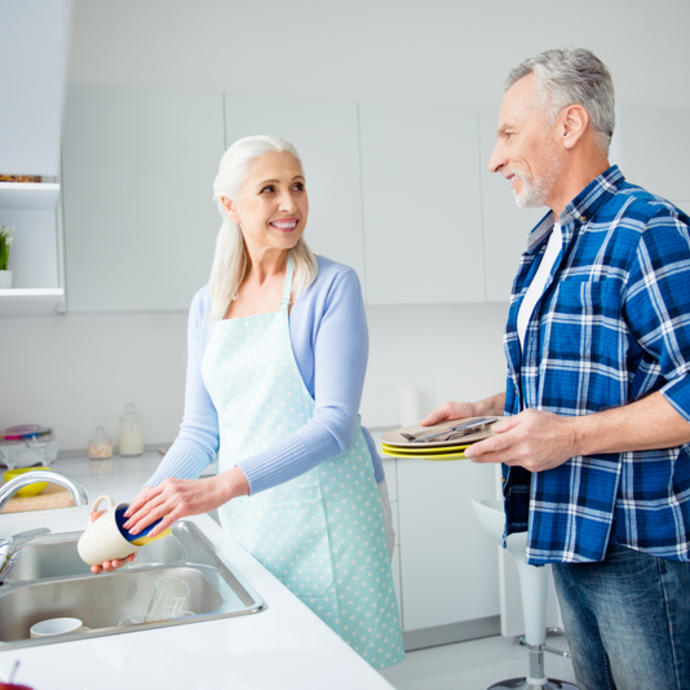 An older husband and wife wash dishes together in the kitchen