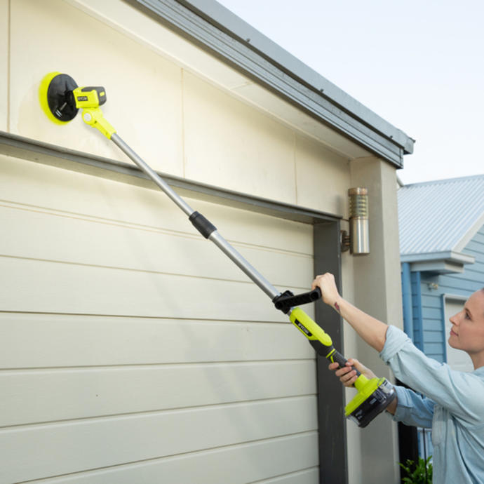 A woman uses a RYOBI telescopic scrubber to clean the outside of a garage