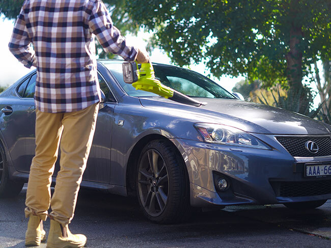 A man using a RYOBI garden blower to clear debris from the bonnet of a car. 