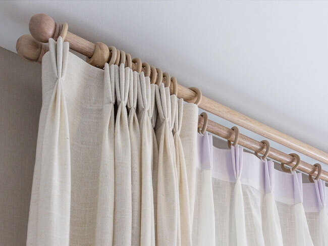 A closeup on the upper section of cream linen curtains hung on timber tods, showing them to be clean and tidy. 