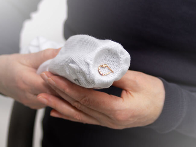 A closeup of a sock placed over the suction hose of a vacuum, being used to retrieve an earring without it being sucked up. 