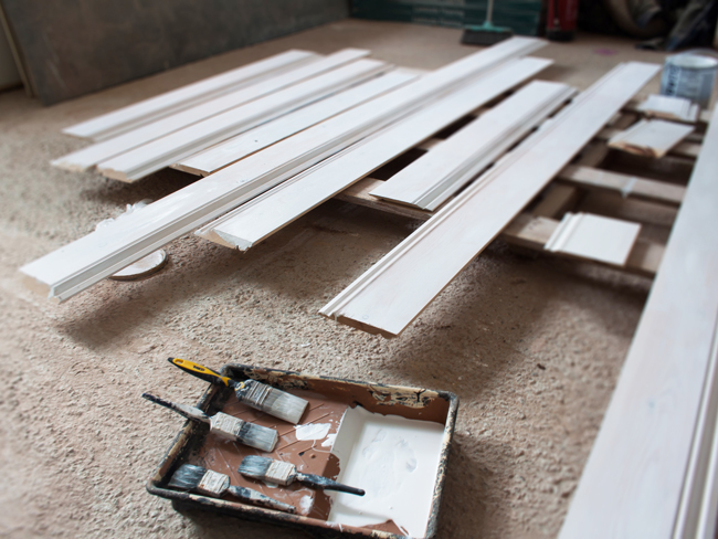 Freshly painted skirting boards laid out to dry on the floor, next to a paint tray with paint brushes. 