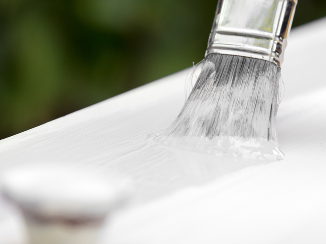 A closeup of a paint brush being used to apply a clear varnish to a white painted surface. 