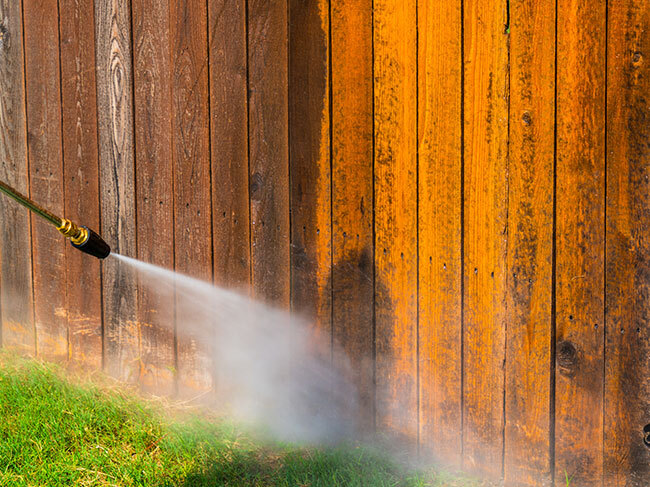 A RYOBI pressure washer being used with a turbo nozzle to remove a buildup of grime from timber fence slats. 