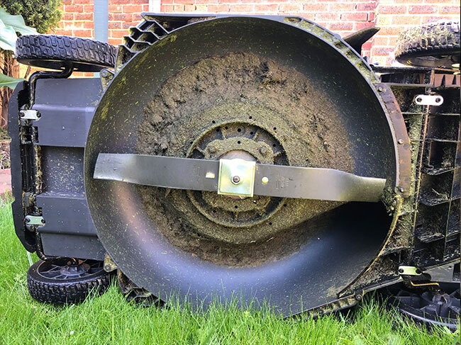 The underside of a RYOBI lawn mower, showing it to be covered in grass clippings. 