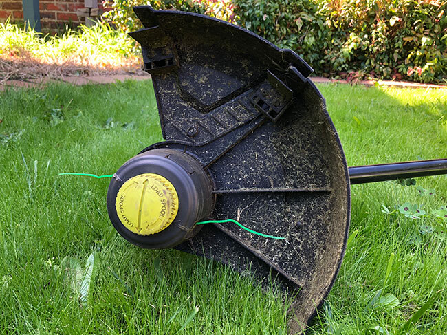 The underside of the safety guard from a RYOBI line trimmer, showing it to be covered in grass clippings. 