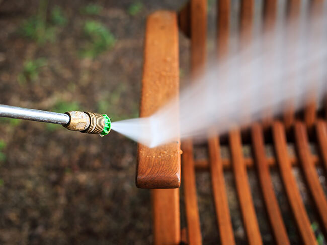 A closeup of a RYOBI pressure washer being used with a 25 degree nozzle to clean a jarrah deck chair. 