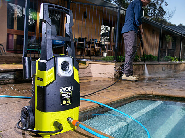 A man using a RYOBI pressure washer to clean the concrete pavers around the edge of a pool. 
