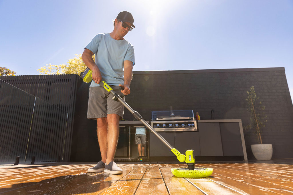 A man uses a RYOBI 18V ONE+ Telescopic Power Scrubber to clean his deck