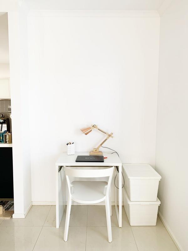 A small white desk with a lamp and two storage tubs