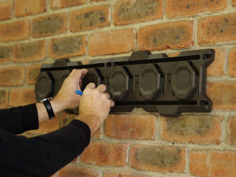 Hands marking drill hole on brick wall using LINK storage system as a guide. 