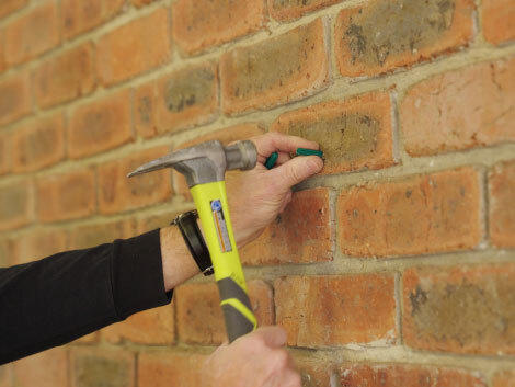 Hands hammering green wall plugs into brick wall. 