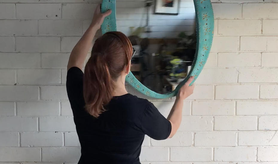 Natasha hanging the finished mirror on a white brick wall