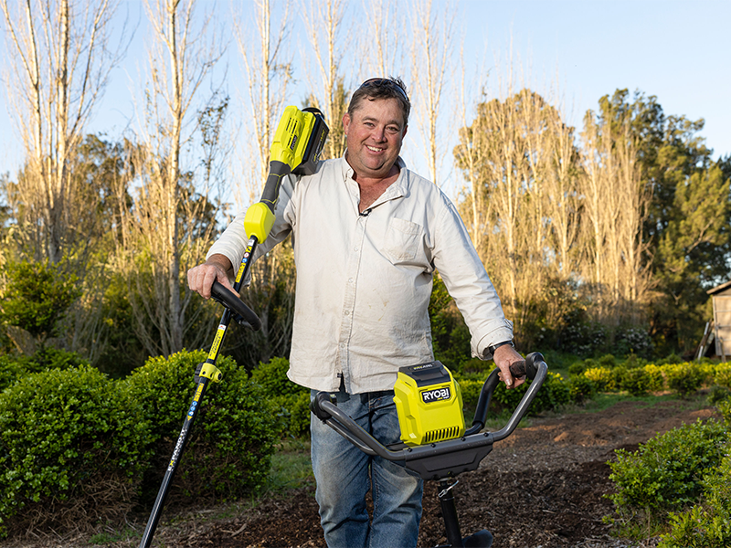 Jason Hodges stands in the garden holding a RYOBI digging tool and cultivator