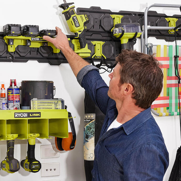 A man in a blue shirt reaches up to add a RYOBI battery to his LINK wall storage
