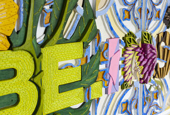 Close up of Be Inspired wooden wall art wording containing bright colours and flower patterns 