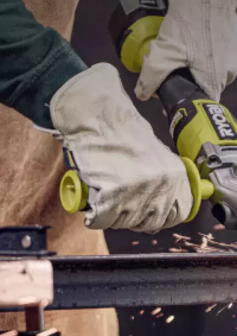 Person using RYOBI angle grinder on metal bar with sparks flying