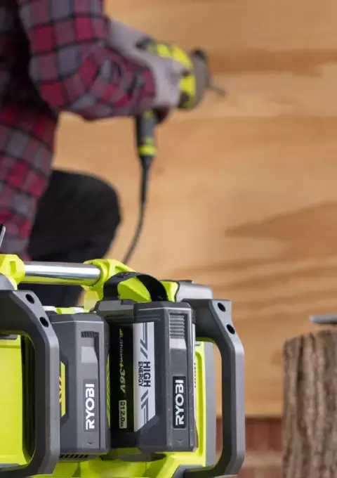 RYOBI portable power station in foreground, with person drilling blurred in background 
