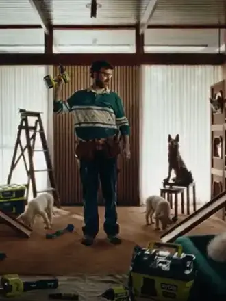 A man stands holding a RYOBI drill surrounded by dogs