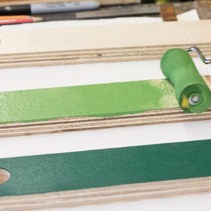 Using a roller to paint planks of wood different shades of green